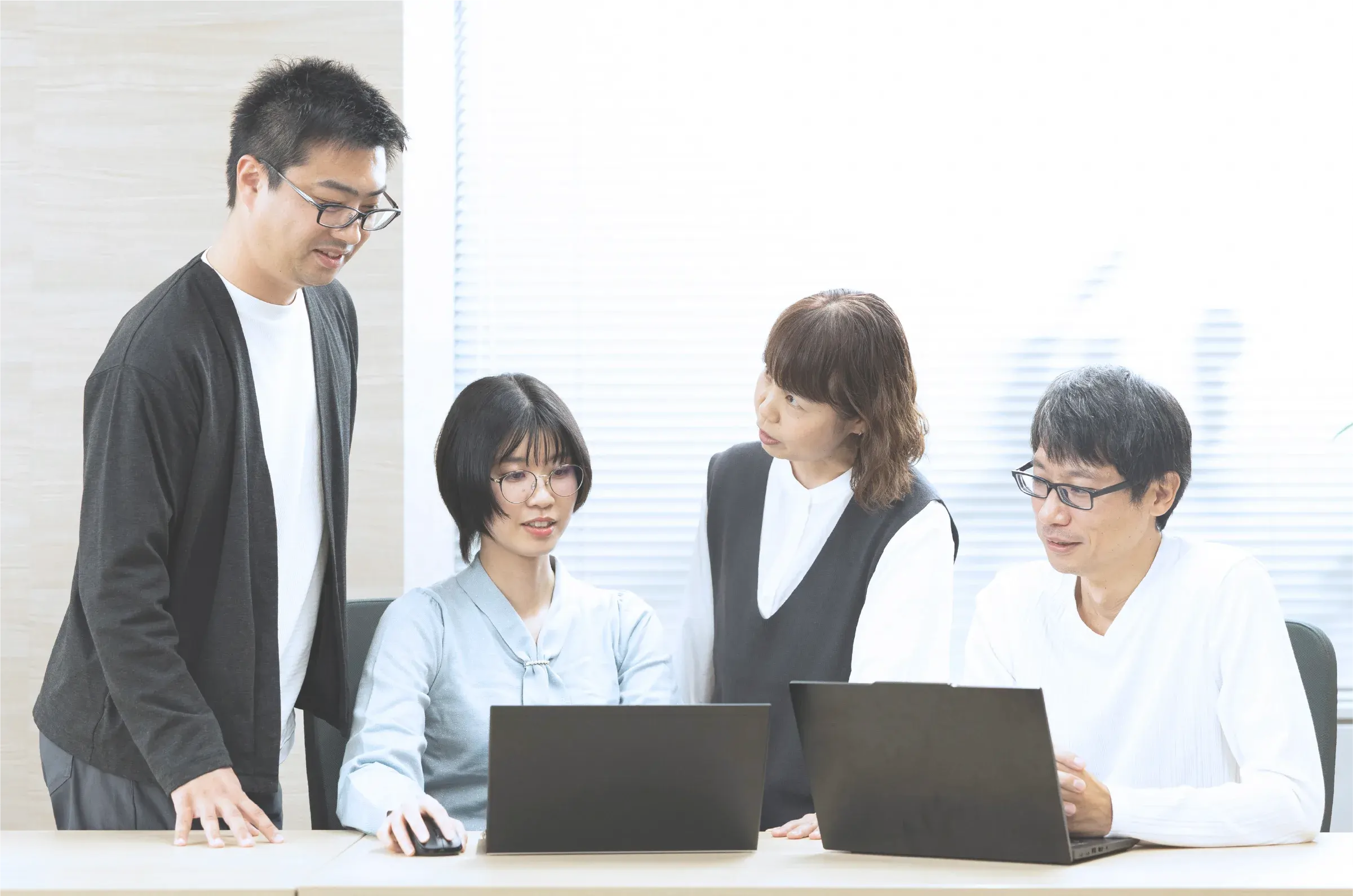 4人の社員がノートPCを見ながら打ち合わせをしている様子